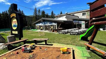 A dirt play area with toy vehicles, a wooden bench, and a picnic table. In the background, there's a building with a sign that reads "Restaurant."