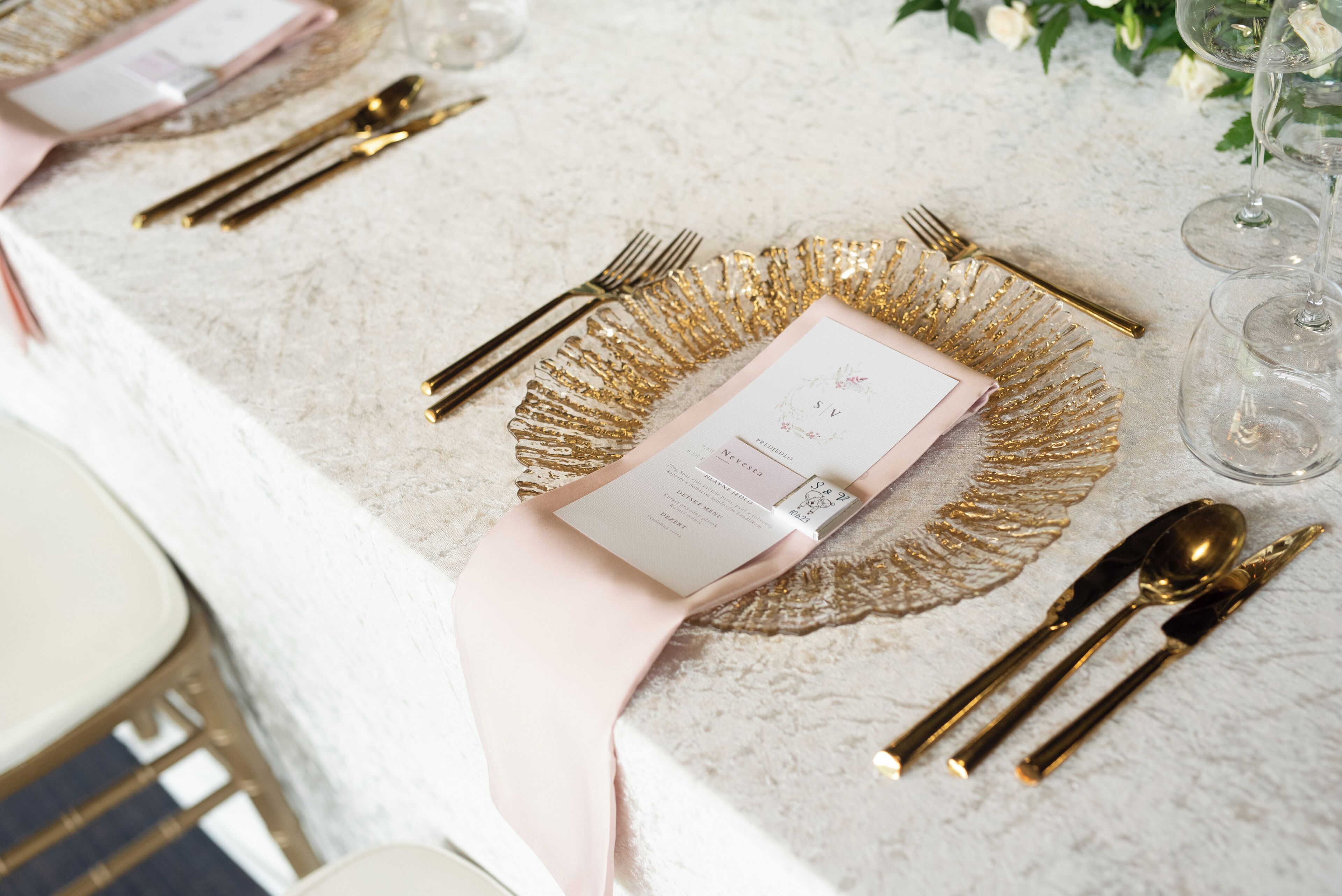 Una mesa puesta con cubiertos dorados, una servilleta rosa y un menú.