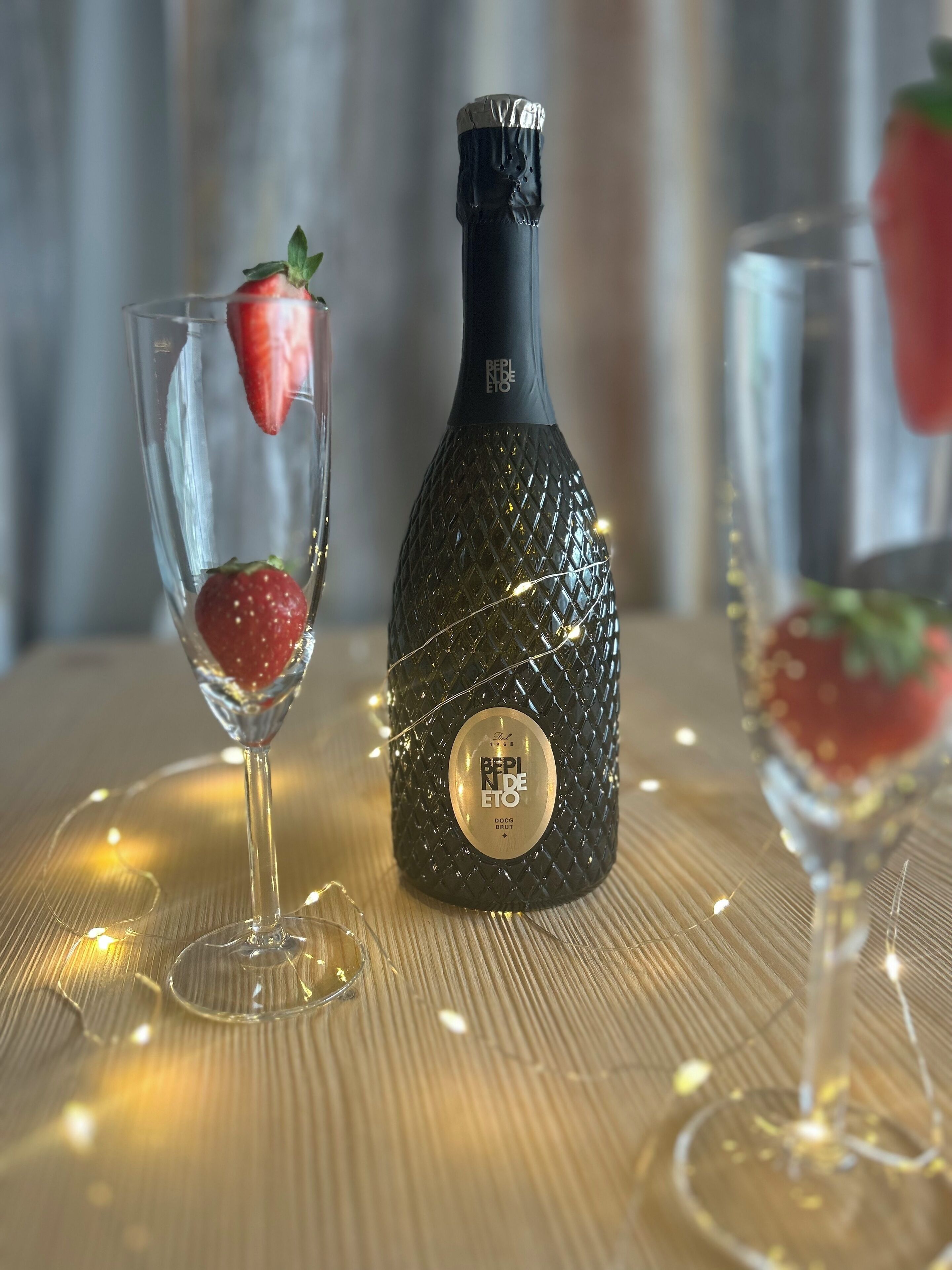 Uma garrafa de BePino de Eto DOC Brut com etiqueta, colocada sobre uma mesa com dois copos contendo morangos.