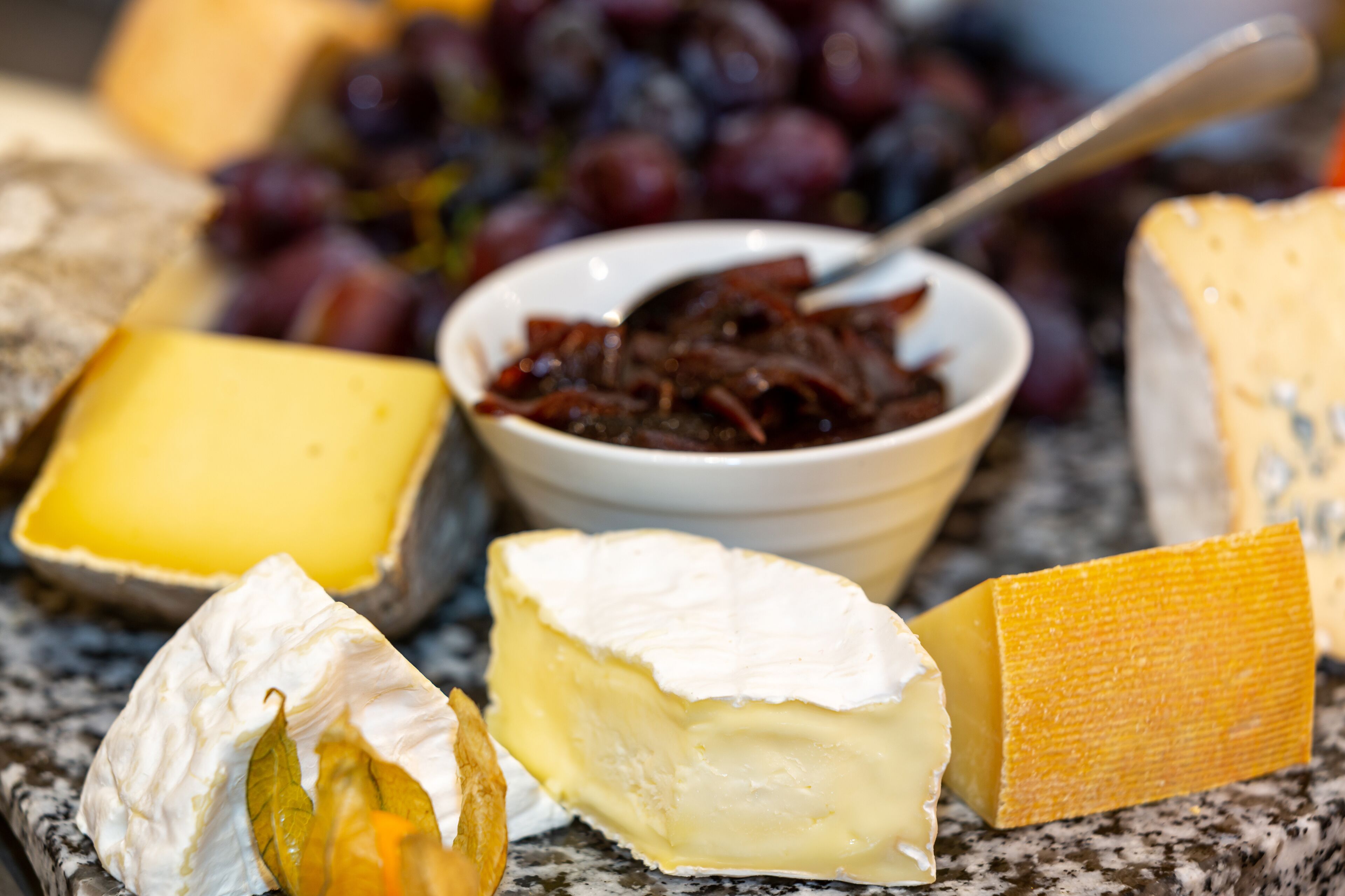 A selection of cheeses and grapes on a marble surface.
