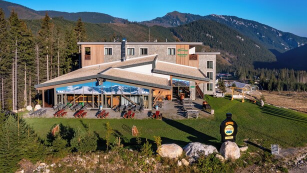 Een modern gebouw met een bar en restaurant, omgeven door bergen en bomen.