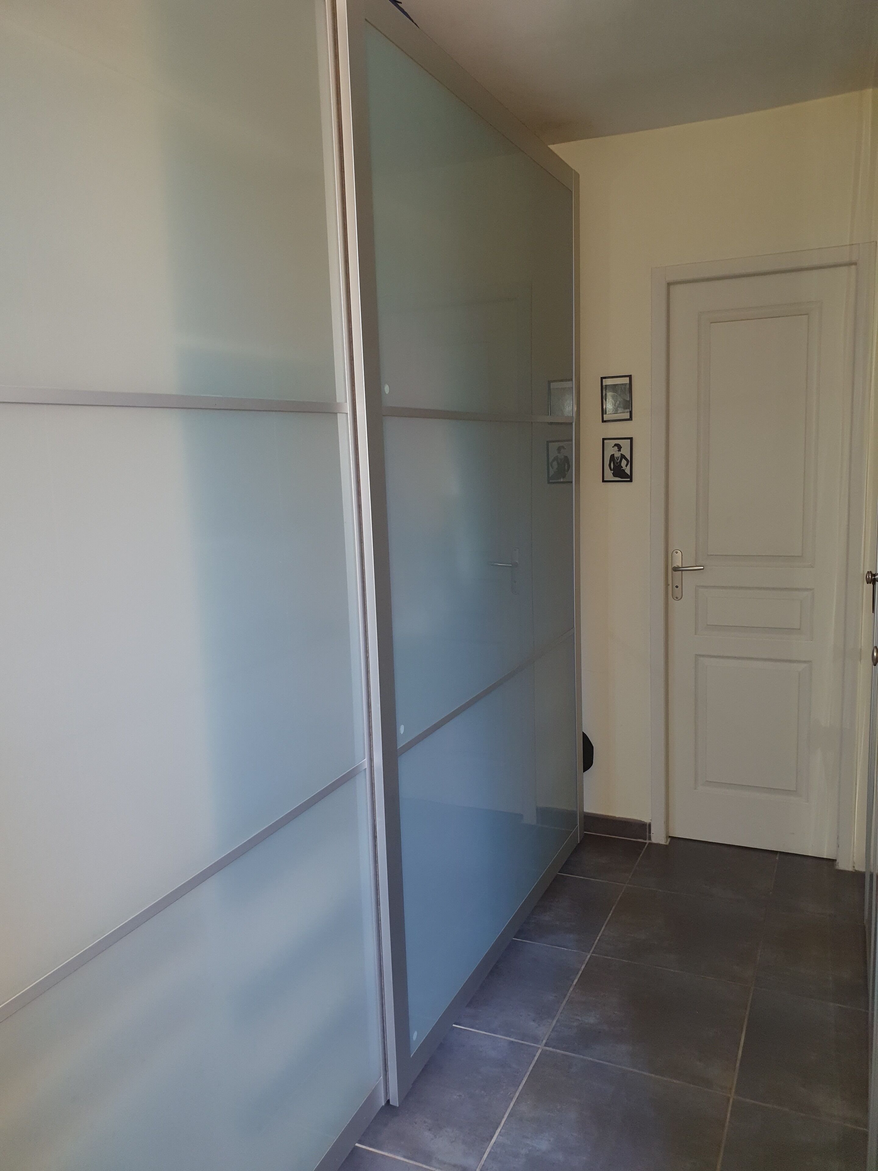 Un couloir avec une porte coulissante en verre, une porte blanche et un sol carrelé.