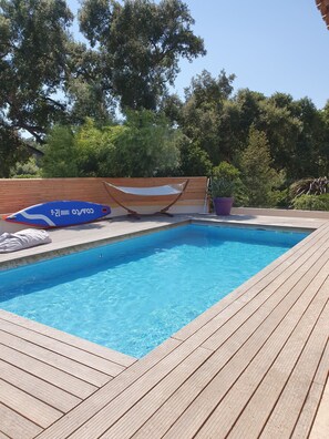 A swimming pool with a wooden deck, a hammock, and a potted plant. - Beautiful, modern house with a pool near the ocean (Le Pradet)