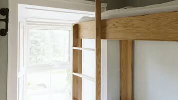 A bunk bed with a wooden frame and white bedding, a window with white blinds, and a white wall.