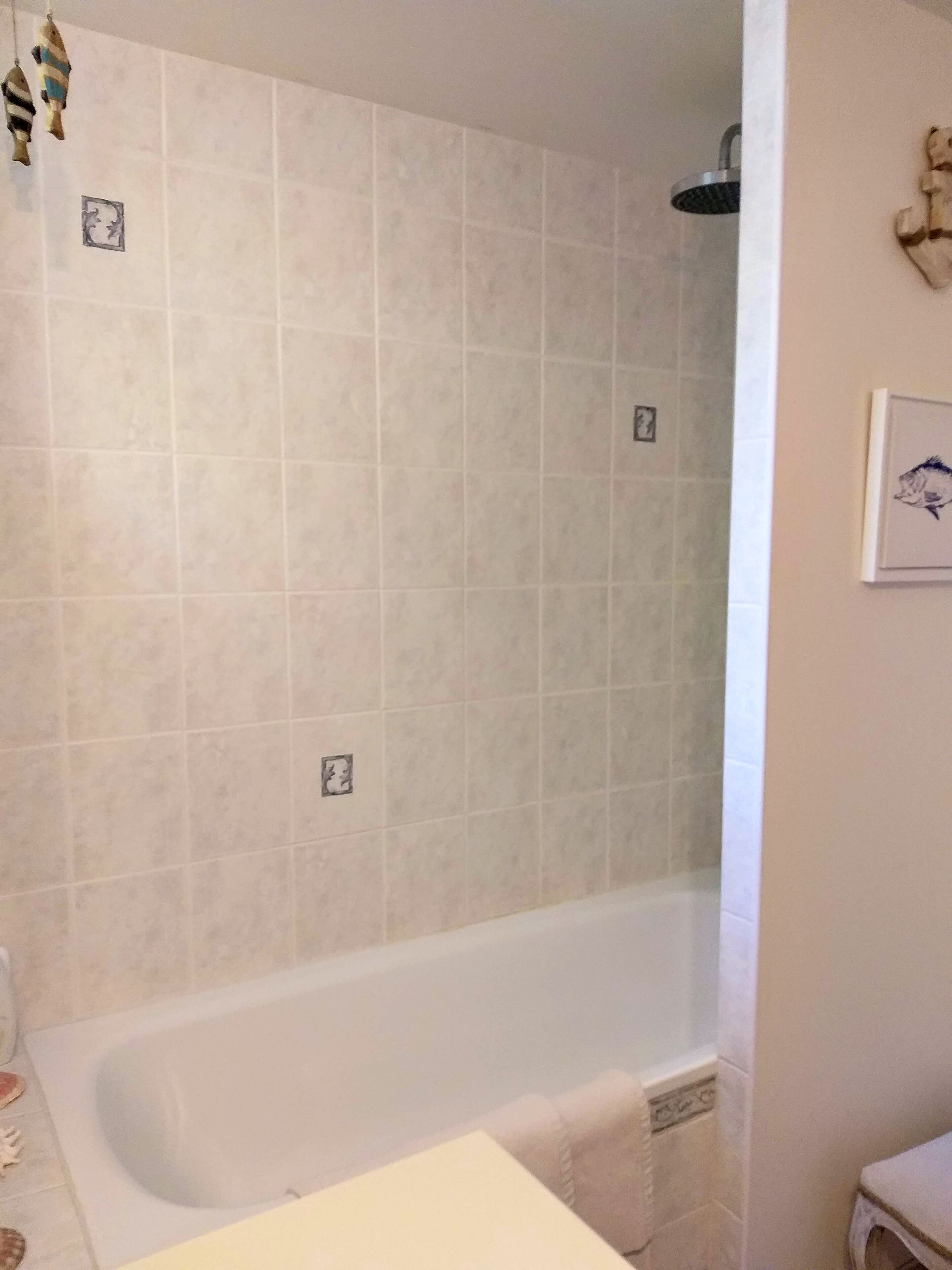 Un baño con bañera, paredes de azulejos, cabezal de ducha y un cuadro en la pared.
