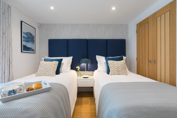 A hotel room with two beds, a nightstand, a tray with breakfast items, and a large wooden wardrobe. - Gwel An Chapel (St Ives)