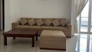 A modern living room with a beige sofa, striped cushions, a wooden coffee table, and a matching ottoman. - Short Term Apartment in Colombo City  (Colombo)