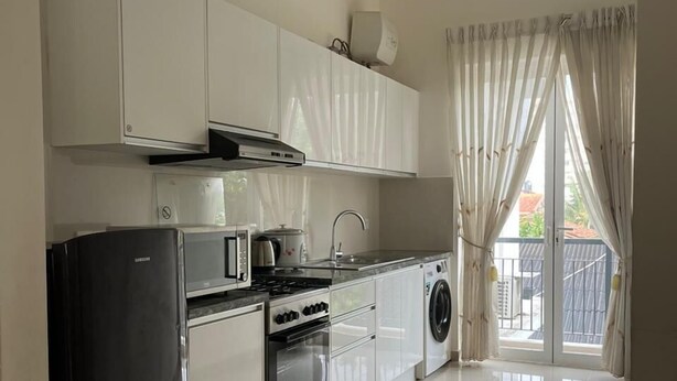 A modern kitchen with white cabinets, a black refrigerator, a microwave, an oven, and a washing machine. - Short Term Apartment in Colombo City  (Colombo)