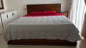 A neatly made bed with a white and red bedspread, a wooden headboard, and a white nightstand with a lamp. - Short Term Apartment in Colombo City  (Colombo)