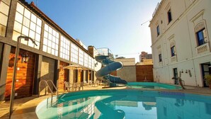 A swimming pool with a slide, surrounded by buildings with large windows and a clear sky. - Palace Hotel de Caxambu (Caxambu)