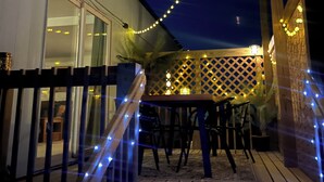 Um deck externo com guarda-corpo de madeira, uma mesa e cadeiras.