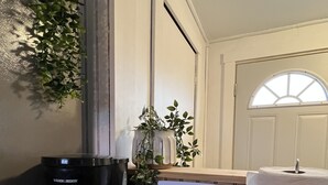 Uma bancada de cozinha com uma cafeteira, um recipiente cerâmico branco, um rolo de papel toalha e uma planta em vaso.