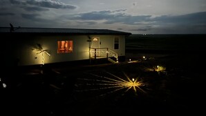 Uma casa com escadas que levam à entrada, um alpendre iluminado por luzes e vista para a paisagem ao redor.