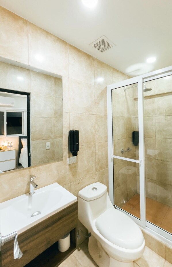 A modern bathroom with a large mirror, a sink, a toilet, and a glass-enclosed shower.