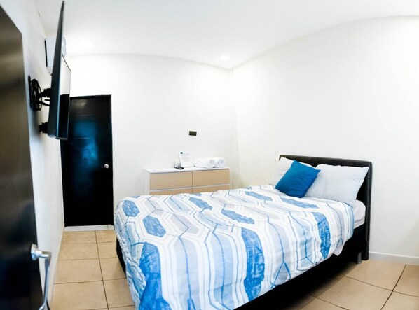 A bedroom with a bed, a nightstand, a TV mounted on the wall, and a door. - Amaremar (San Luis Talpa)