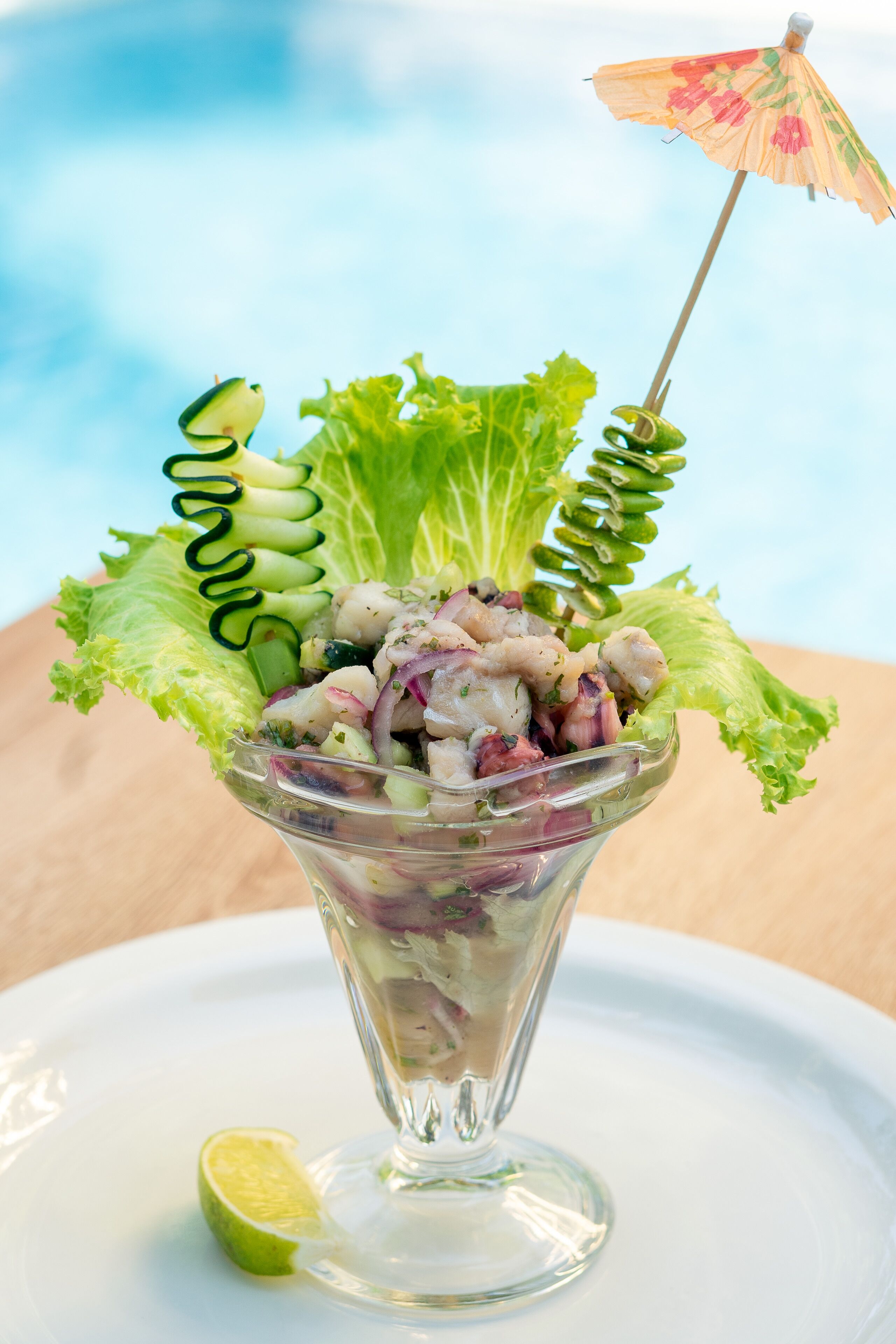 Een salade in een glazen schaal, met een limoenpartje en een decoratieve paraplu.