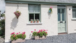 A white building with a green door and windows, potted plants, and a gravel driveway.