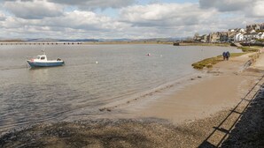 A coastal scene with a boat docked near the shore, a sandy beach, and a bridge in the background.