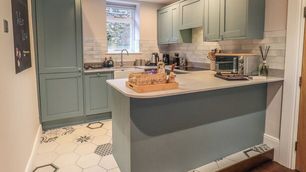 A modern kitchen with teal cabinets, a central island, and a window providing natural light.