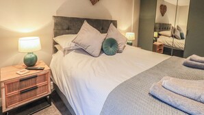 A modern bedroom with a large bed, a bedside table with a lamp, a mirror, and a heart-shaped decoration on the wall.