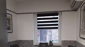 Une petite cuisine avec une table en bois et deux chaises, une fenêtre avec des stores à rayures et une plante en pot posée sur le rebord de la fenêtre.