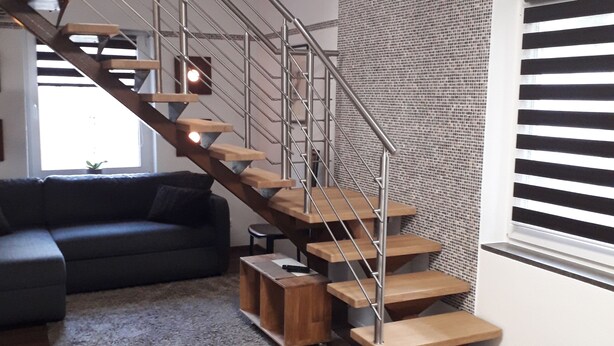 Un salon moderne avec un escalier en bois, un canapé gris et un mur orné de motifs.