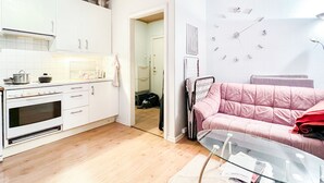 Una cucina moderna con mobili bianchi, un fornello e un'area pranzo con tavolo in vetro e divano rosa.