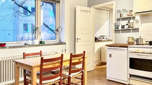 Una cucina con un tavolo e sedie in legno, una finestra con persiane, un frigorifero bianco e un fornello.