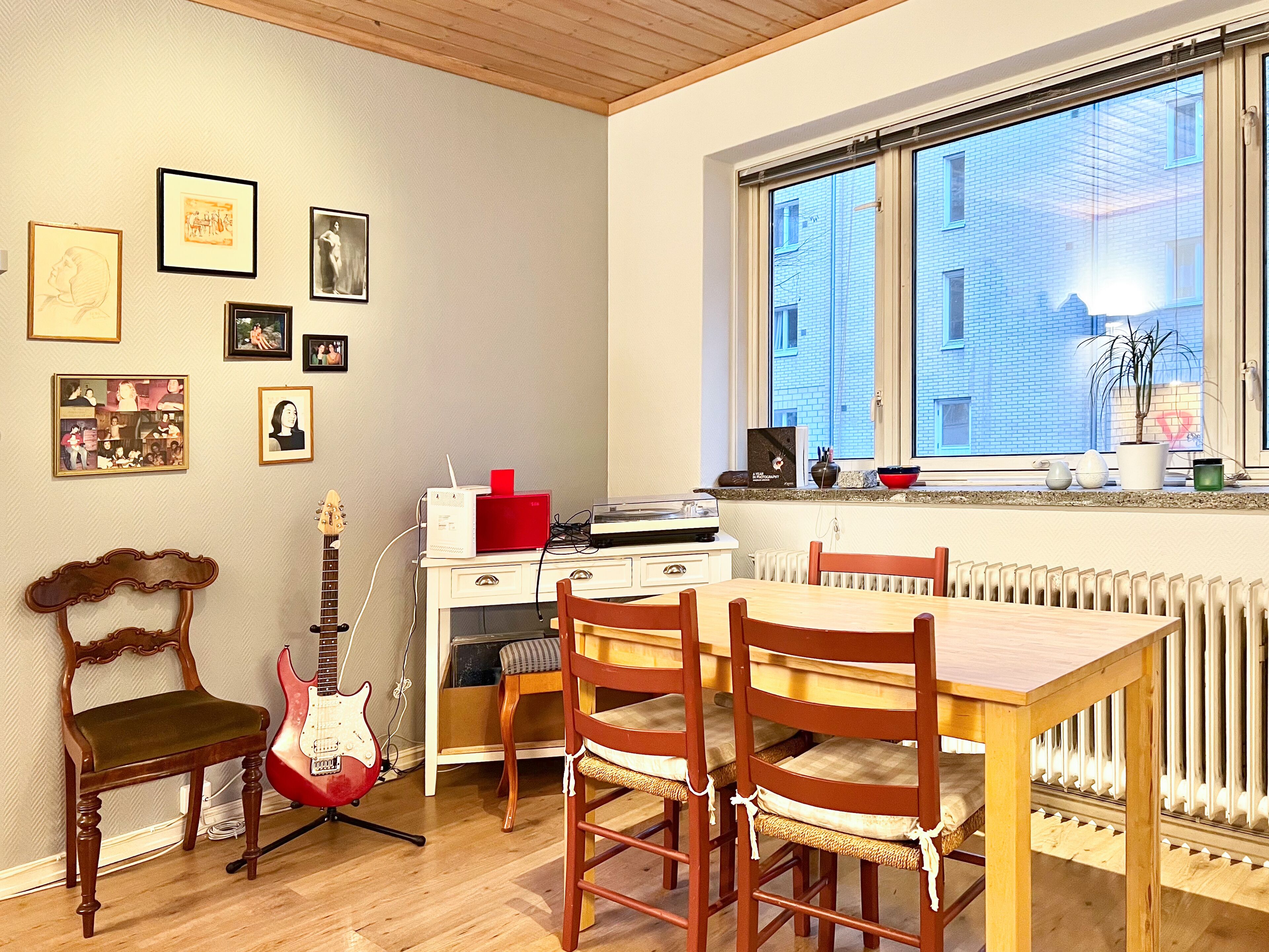Ein Zimmer mit Esstisch, Stühlen, einer Gitarre, einem roten Verstärker und gerahmten Bildern an der Wand.