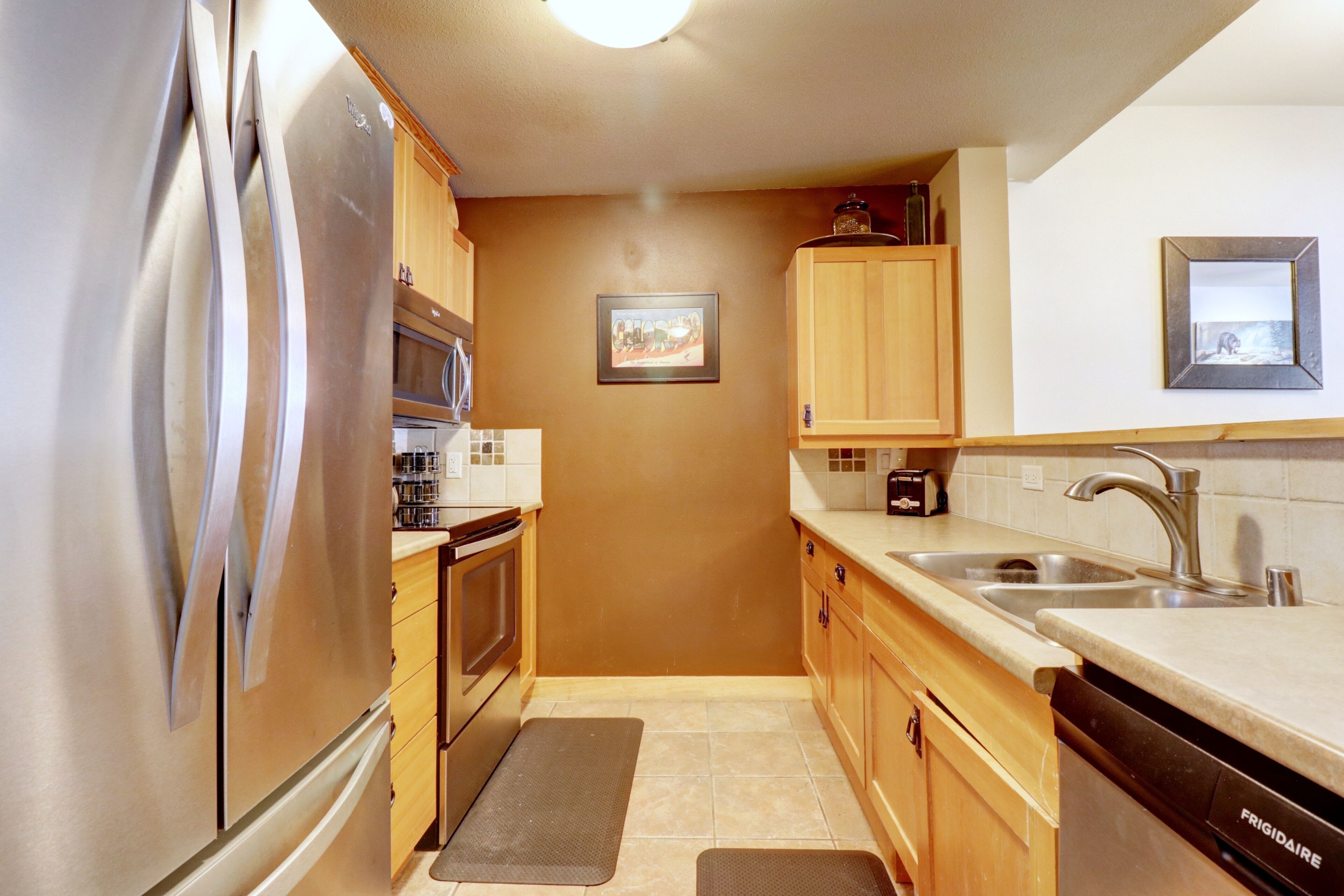 A compact kitchen with stainless steel appliances, wooden cabinets, a dishwasher, and a tiled backsplash.