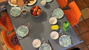 Ein Esstisch mit orangefarbenen Stühlen, eine Fruchtschale sowie verschiedene Geschirrteile und Besteck.