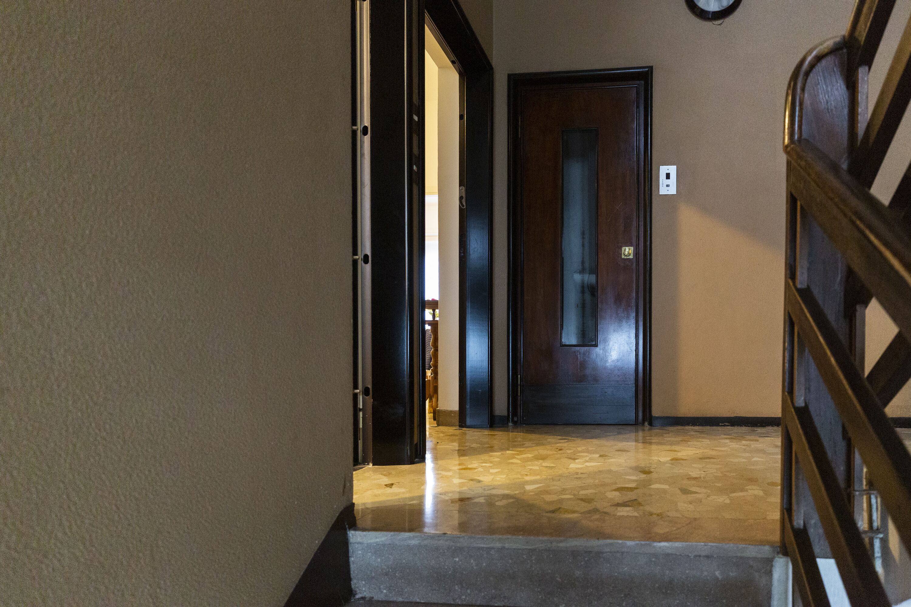 A hallway with a wooden door, a light switch, and a staircase with a metal railing.
