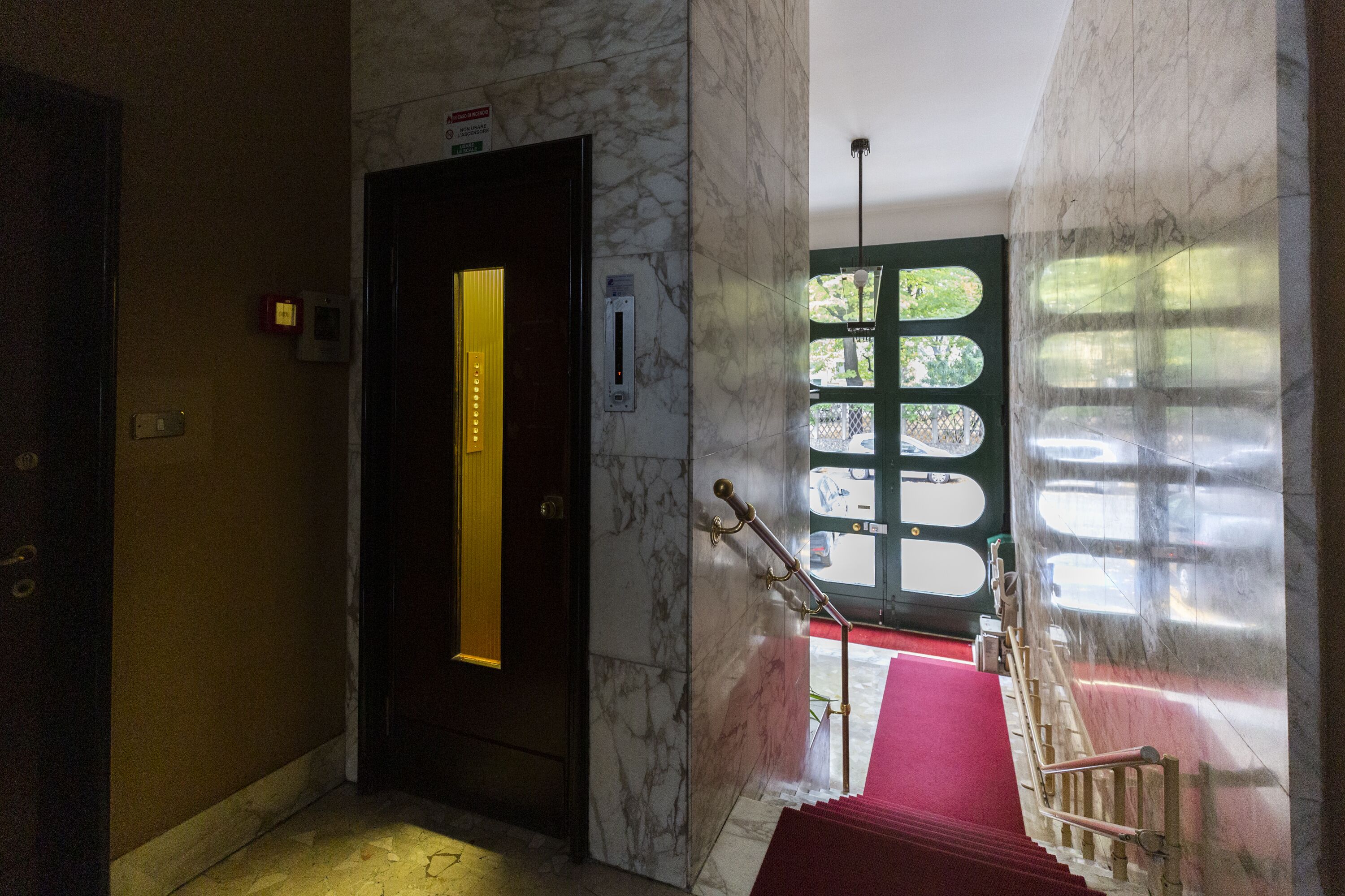 A marble staircase with a red carpet leading to a door with a vertical light strip.
