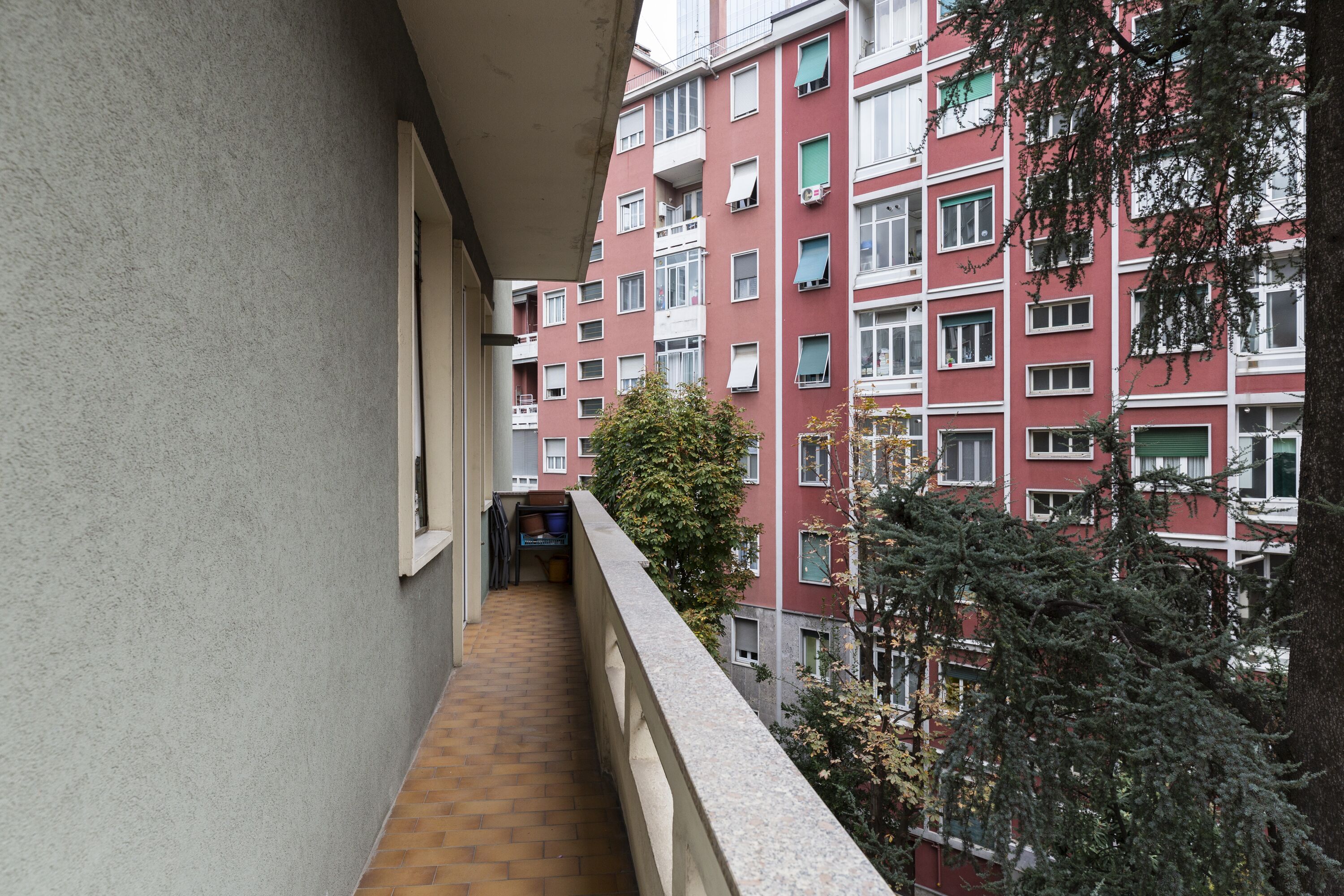 Un balcon étroit, doté d’un sol carrelé, qui donne sur un immeuble rouge avec de nombreuses fenêtres et des balcons.