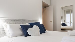 Un lit bien fait, avec des oreillers blancs et bleus, une tête de lit en briques blanches et un mur blanc.