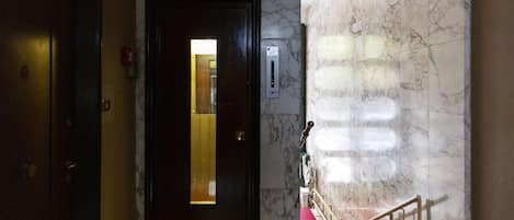 A hotel lobby with a marble wall, a red carpet, and a door with a lighted panel.