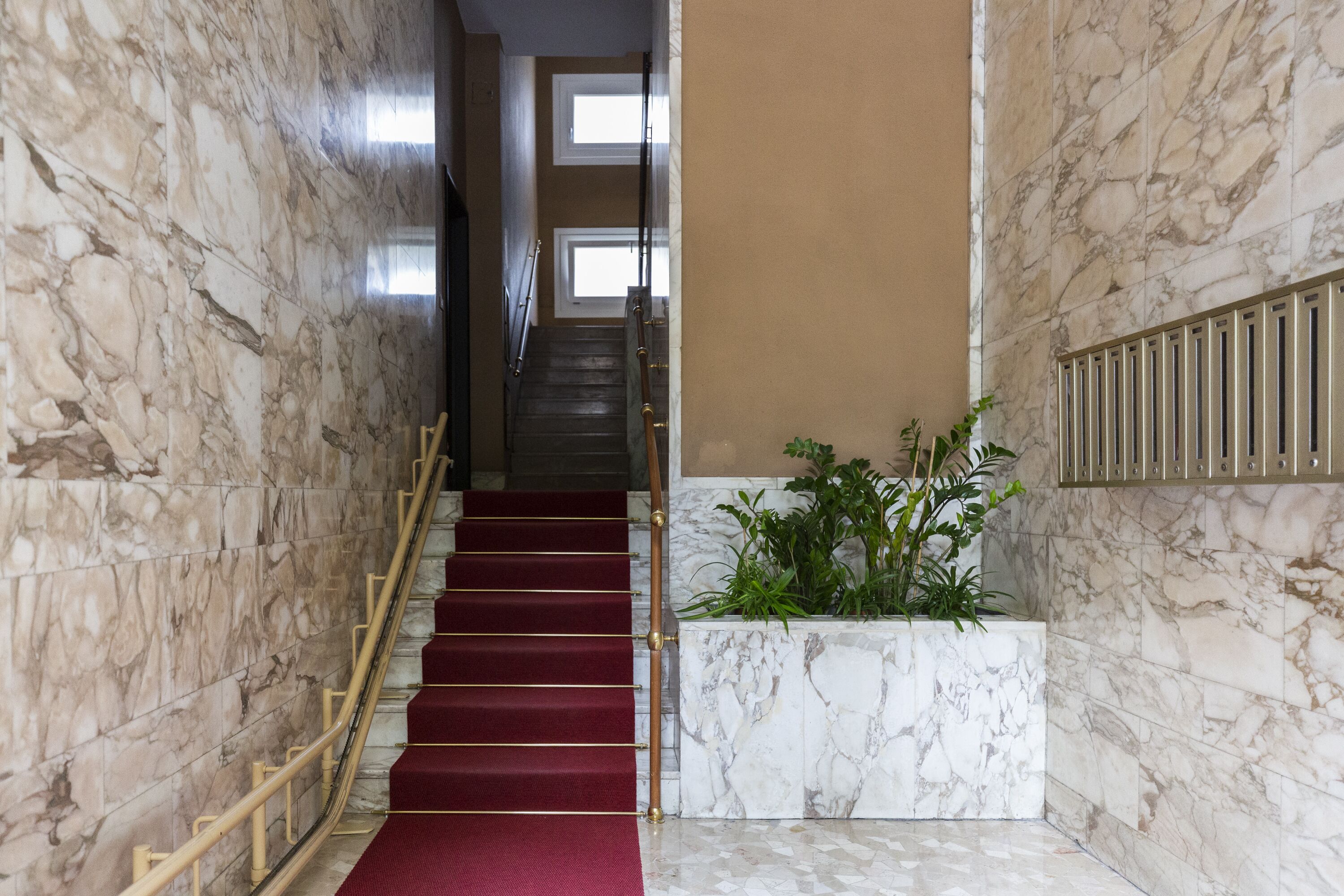A marble staircase with a red carpet and a wooden handrail.