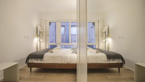Ein Schlafzimmer mit einem großen Bett, Nachttischen, einem Fenster mit Vorhängen und Wandleuchten.