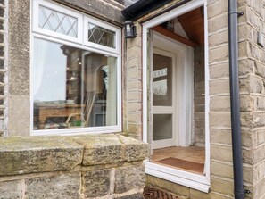A stone building with a white-framed window and a door leading to a tiled entrance.