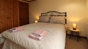 A bedroom with a bed, two bedside lamps, a wooden wardrobe, and a small round table with a lamp. - Rivendell (Holmfirth)