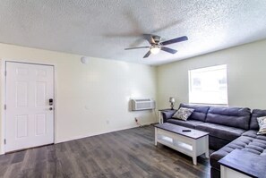 A room with a white door, a ceiling fan, a gray sofa, and a white coffee table.