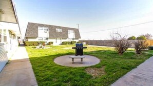 Een achtertuin met een barbecue en een bankje, omringd door een verzorgd gazon en een huis op de achtergrond.
