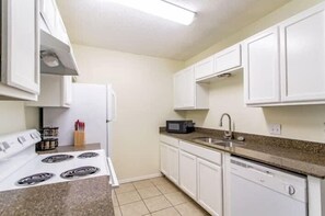 A compact kitchen with white cabinets, a stove, a microwave, and a dishwasher.
