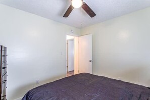 A bedroom with a bed, a ceiling fan, and a door leading to another room.