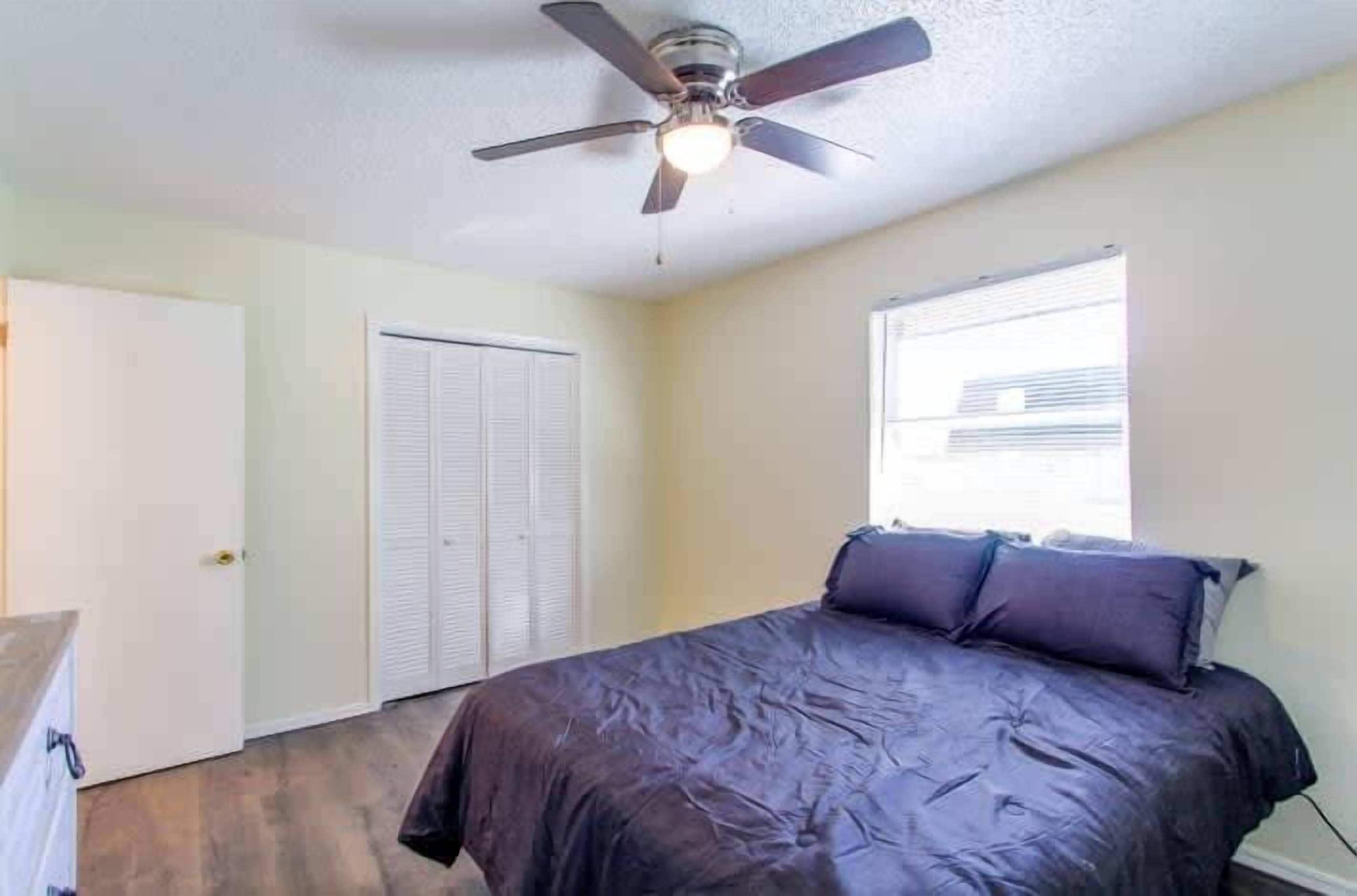 Une chambre à coucher avec un lit, un ventilateur de plafond, une fenêtre et une porte.