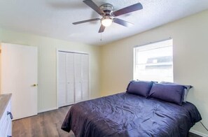 Un dormitorio con cama, ventilador de techo, ventana y puerta.