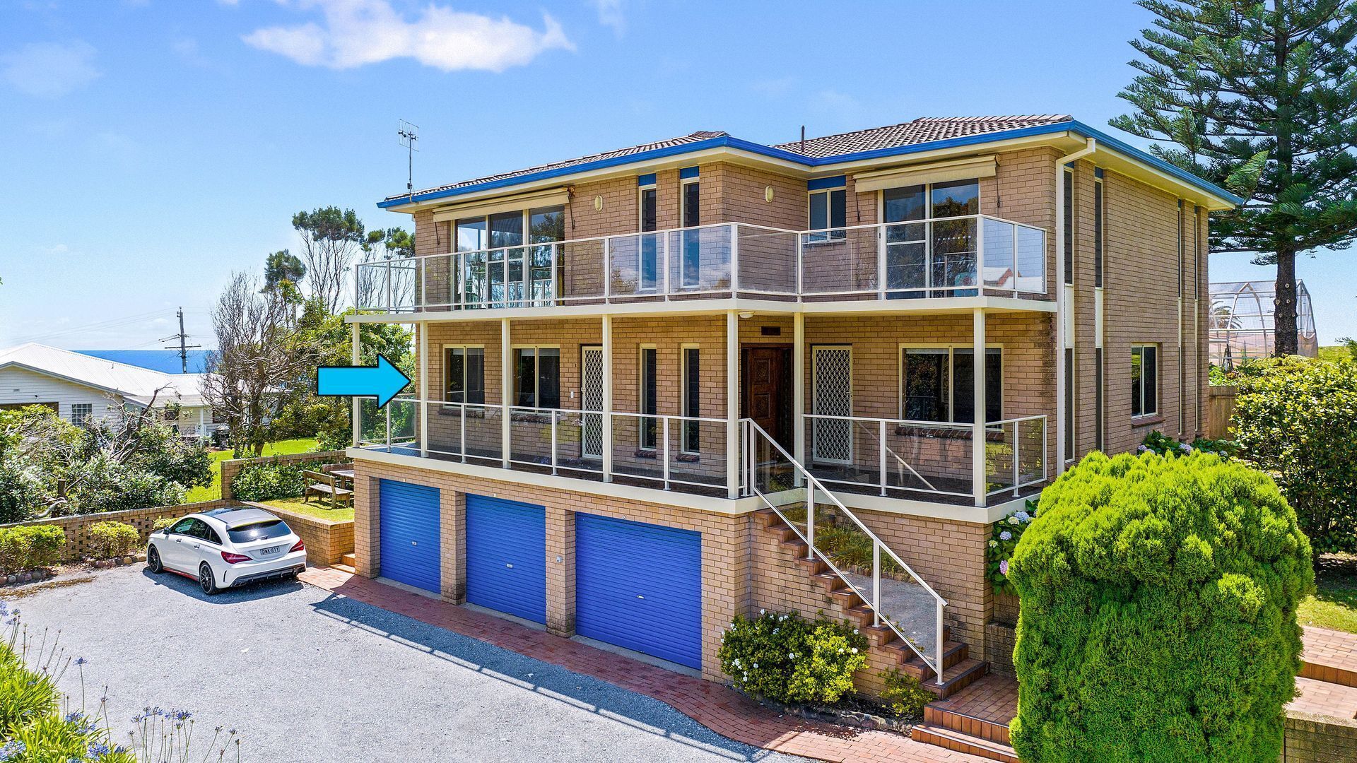 A two-story house with a balcony, a garage with blue doors, and a car parked in front.