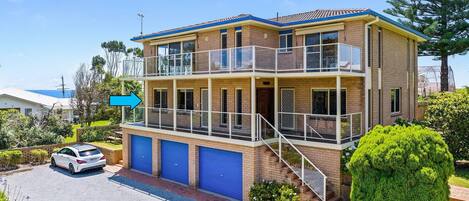 A two-story house with a balcony, a garage with blue doors, and a car parked in front.