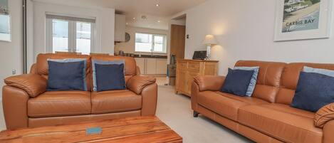A spacious living room with two leather sofas, a wooden coffee table, and a kitchen in the background.
