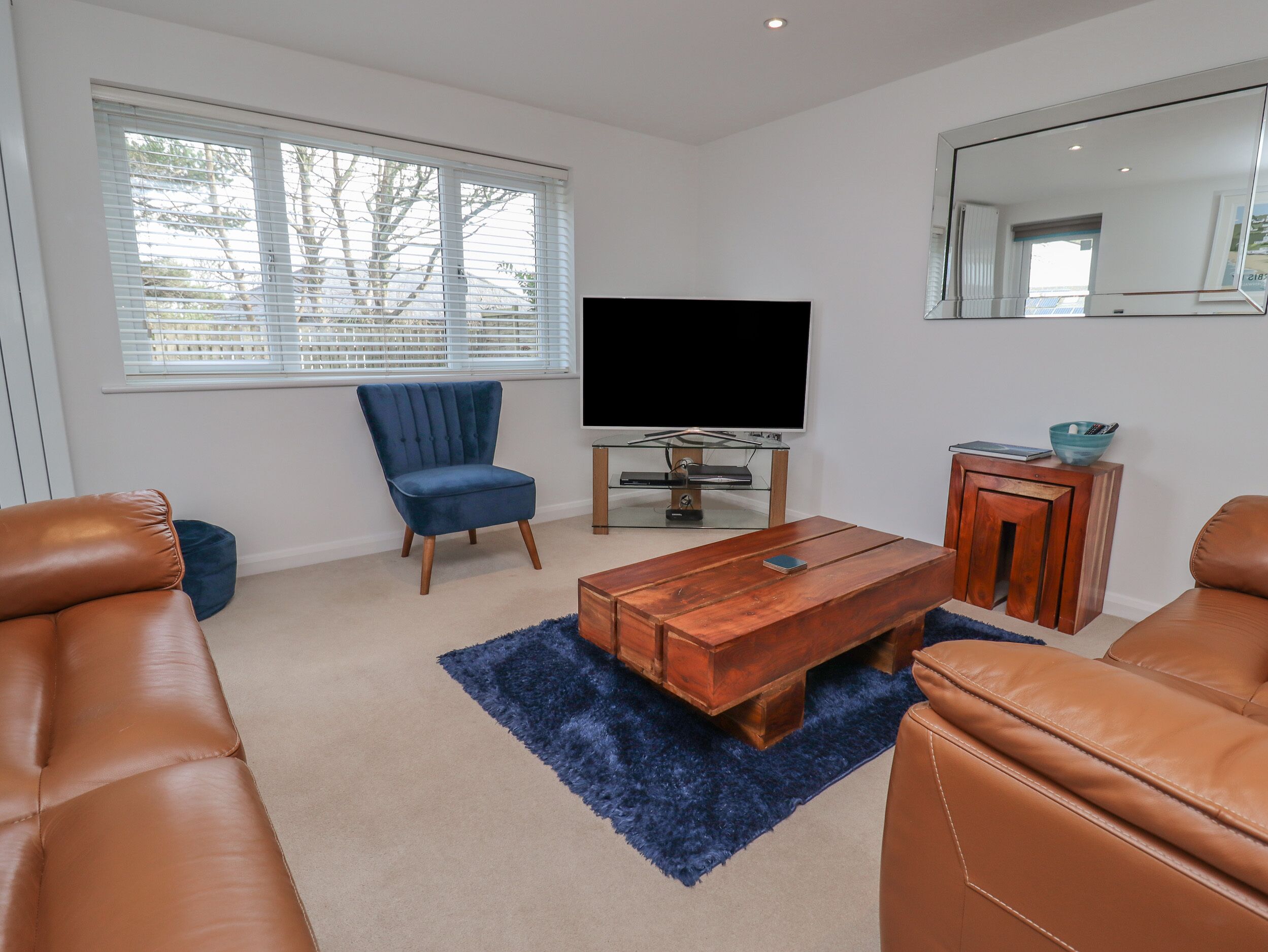 A living room with a TV, a blue chair, a wooden coffee table, and leather sofas.